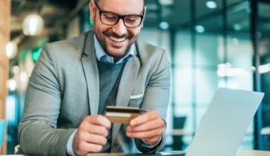 junger Geschäftsmann mit einer American Express Business Gold Card am Laptop