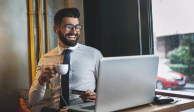 junger Geschäftsmann mit Kaffee und Kreditkarte vor seinem Laptop